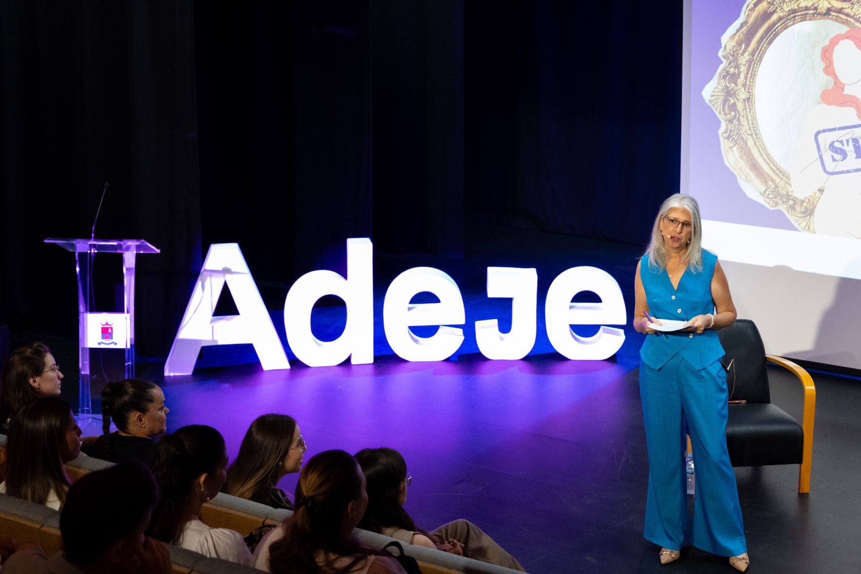 Mónica Radován en escenario con las letras Adeje iluminadas conduciendo un evento institucional