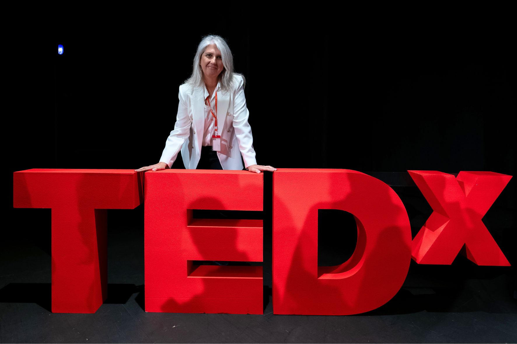 Mónica Radován apoyada sobre las letras corpóreas TEDx en rojo durante el TEDxAdeje 2024